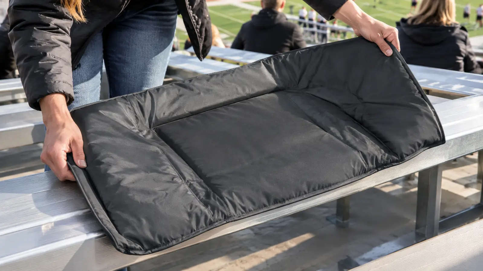 Hands spreading a stadium blanket over a metal bleacher seat at a game