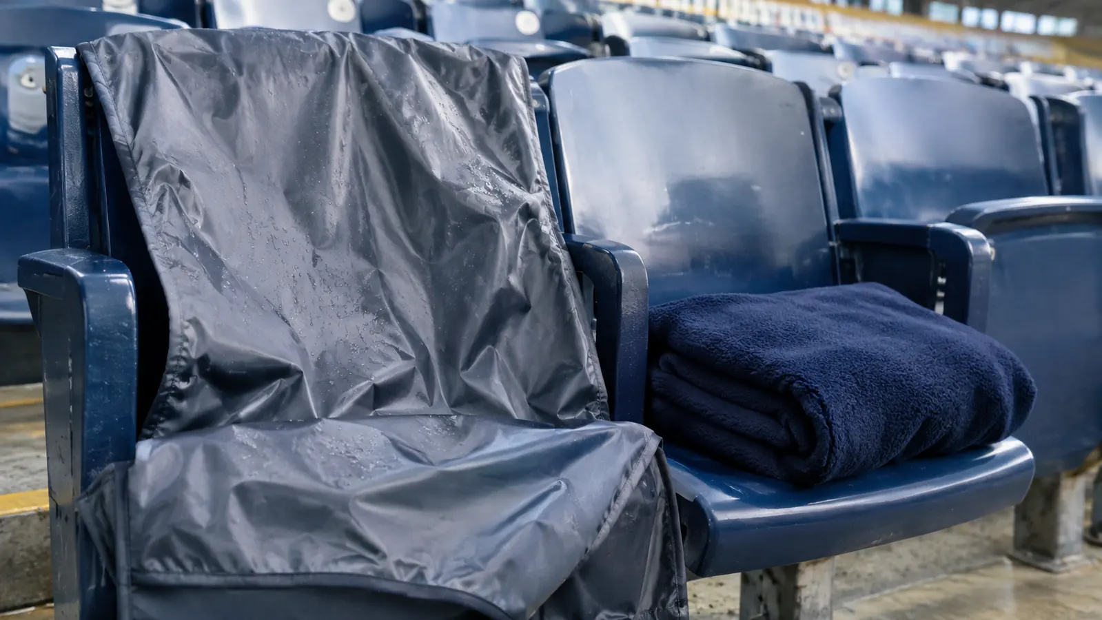 A waterproof stadium blanket draped over a stadium seat, with a regular fleece throw folded beside it