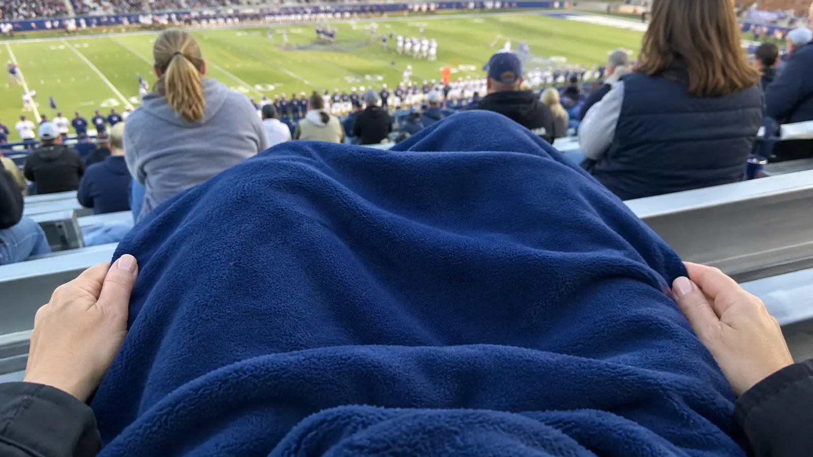 Hands holding a stadium blanket draped over knees in the stands