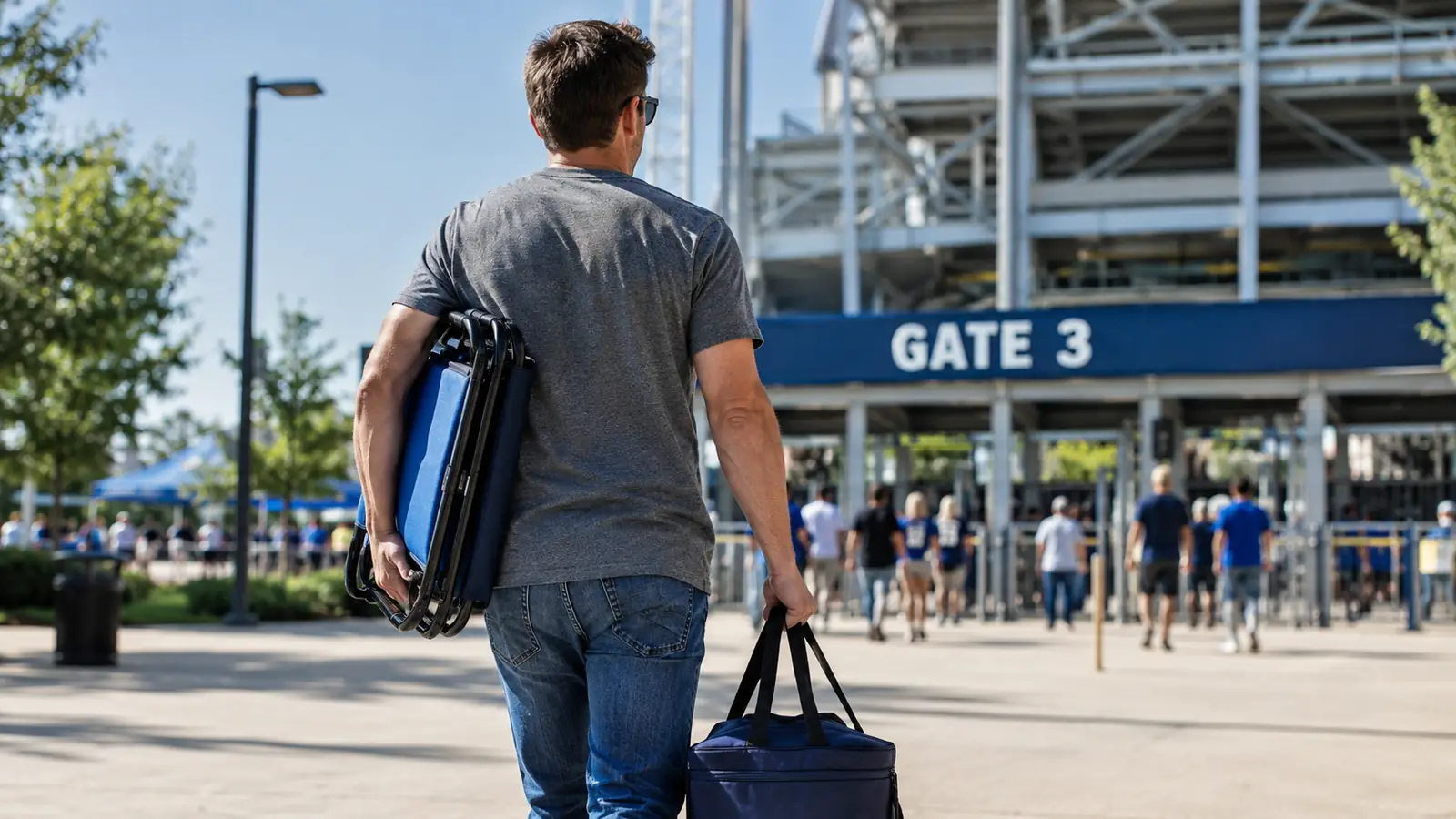 A stadium seat folded flat being carried under one arm while a person walks toward the stadium entrance