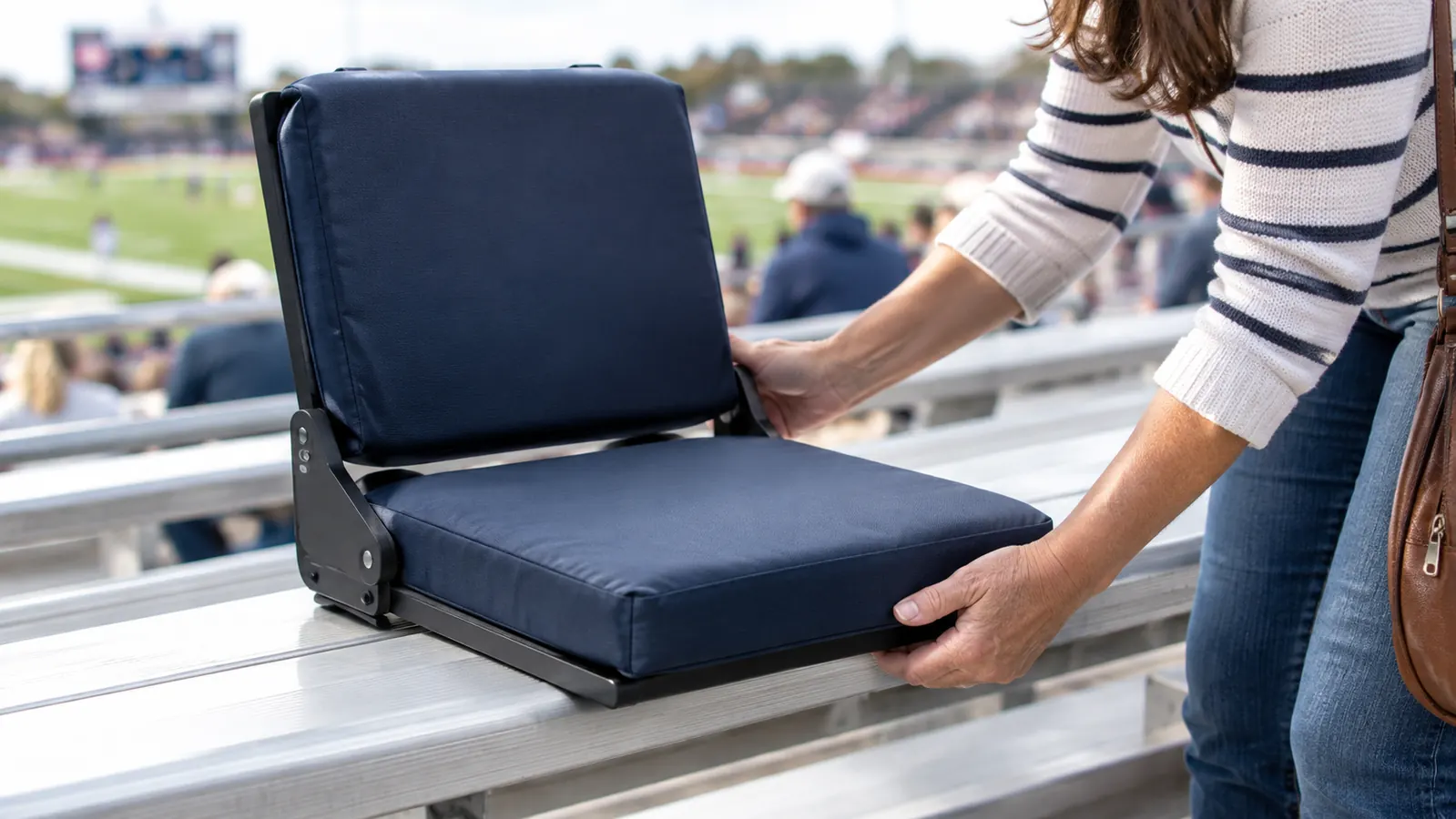 Hands adjusting a padded stadium seat with back support set up on a metal bleacher before a game